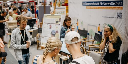 Besuchende an Messestand der KI-Ideenwerkstatt testen Ausstellungsstücke