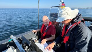 Zwei Personen in einem Boot werten durch Messungen gewonnene Daten aus.