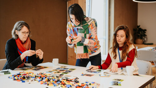 Drei Frauen an einem Tisch, auf dem Legosteine liegen. Sie bauen damit kleine Objekte.