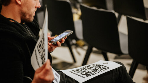 Männlich gelesene Person scannt QR-Code zum Bewerten des Poetry Slams