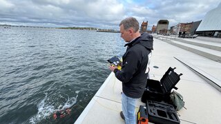 Eine Person steht am Hafenrand und testet eine Unterwasserkamera.