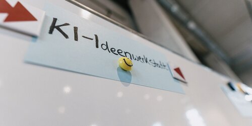 Auf einer Flipchart ist eine Karteikarte mit der Aufschrift "KI-Ideenwerkstatt" gepinnt
