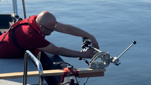 Eine Person sitzt in einem Boot und hält eine Gerät zum Erfassen von Seegraswiesen über das Wasser.